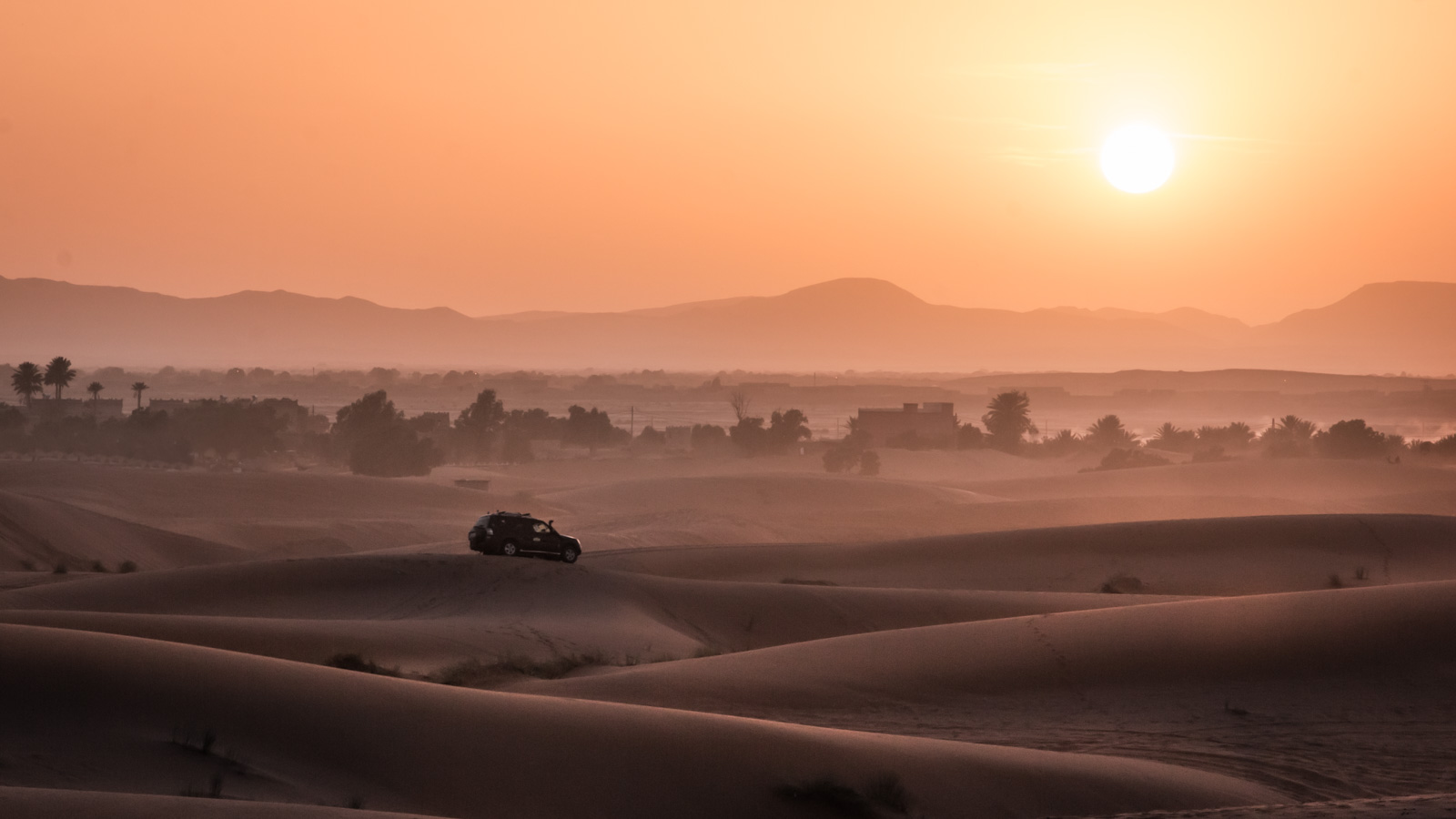 Voiture roule au coucher du soleil dans les dunes du désert au Maroc.